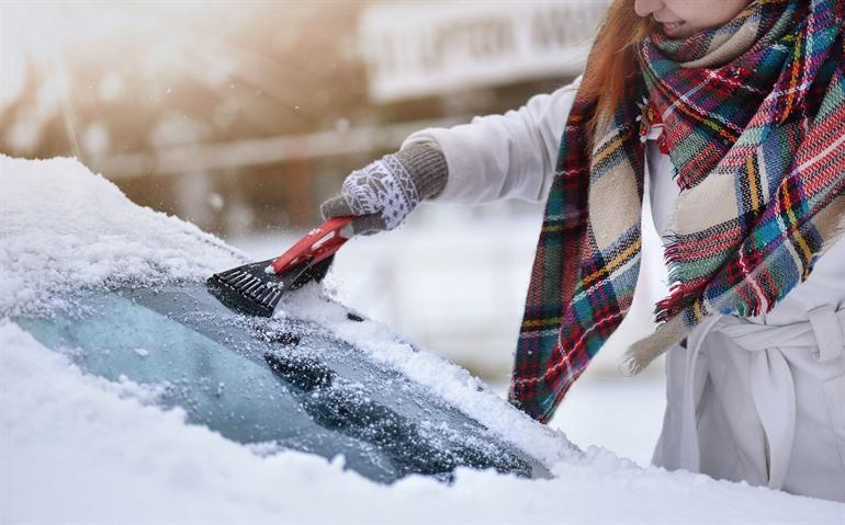 Das Eis von den Autoscheiben mit einem Eiskratzer abkratzen